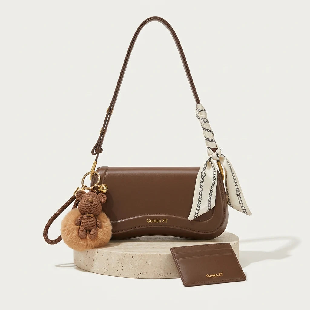 Bolsa de ombro ondulada marrom com o Kit Golden: lenço amarrado na alça, chaveiro de ursinho e porta-cartão