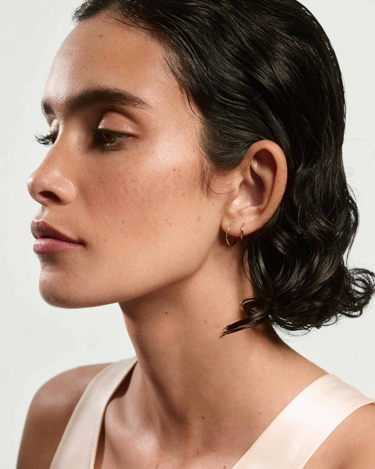 Mulher de perfil usando argola pequena dourada