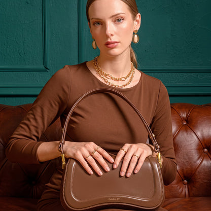 Modelo sentada no sofa com a bolsa de ombro ondulada marrom no colo